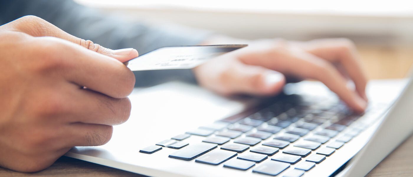 Close-up of male hands holding credit card and typing information on laptop. Businessman making online purchase or booking